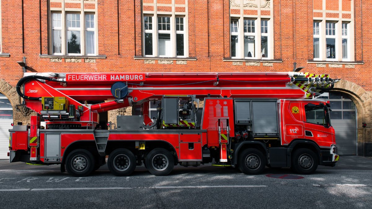 Red fire truck with ladder parked outside a brick building in Hamburg.