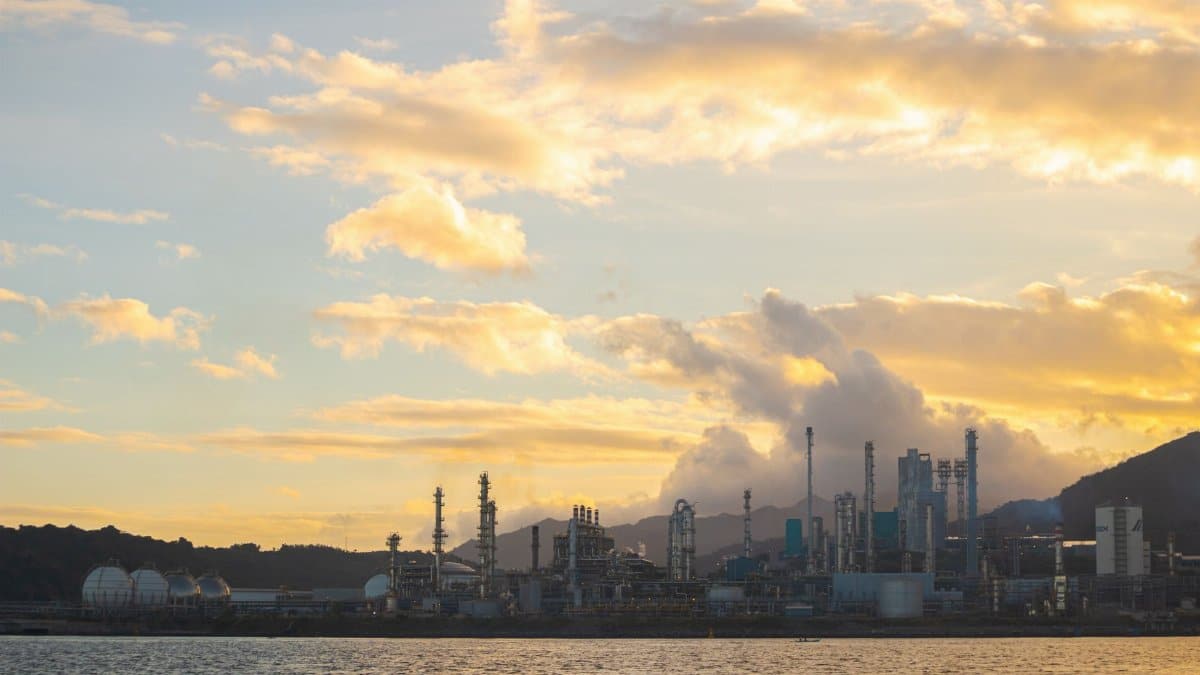 A stunning view of industrial chimneys and skyline with smoke at sunset over the water.