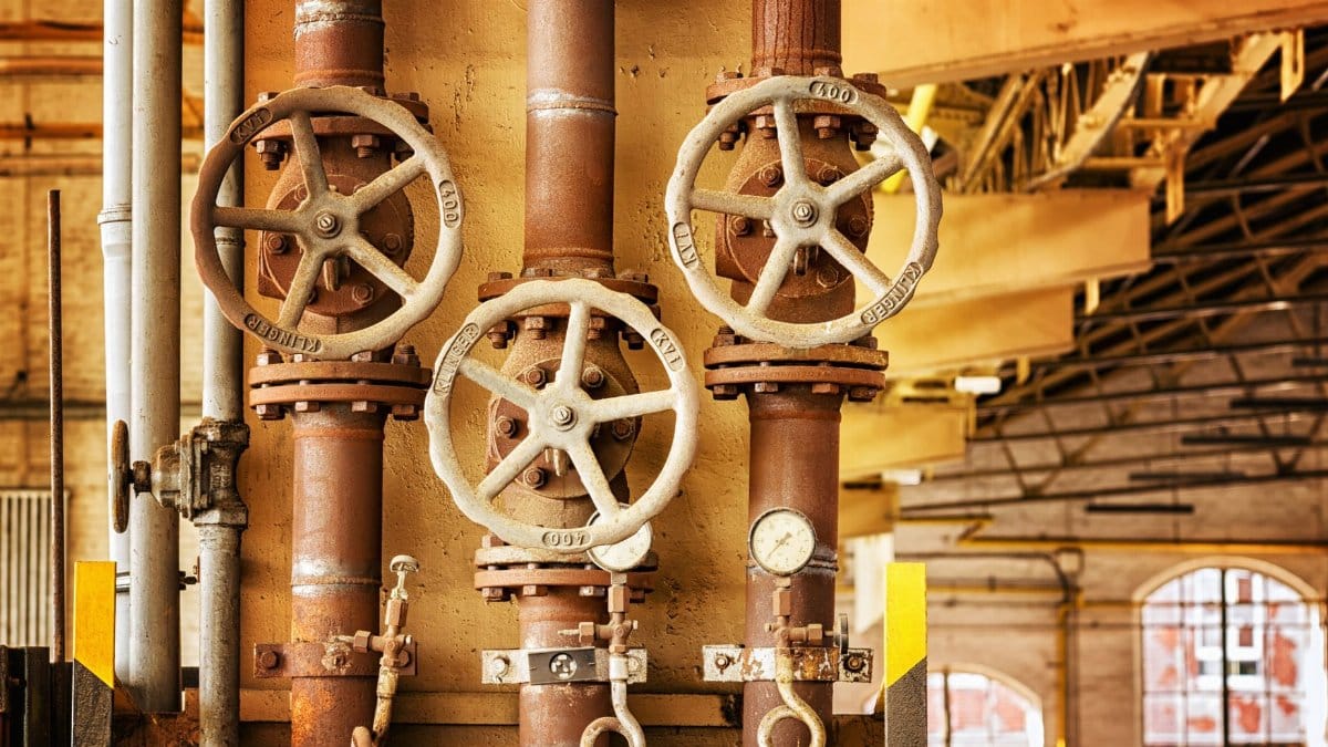 Close-up of rusty industrial pipes and valves, showcasing aging machinery in a factory setting.