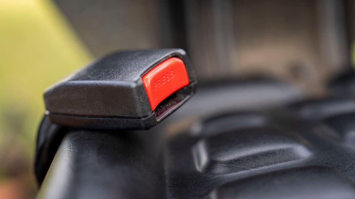 A detailed close-up image of a car seat belt buckle showing the red press button.