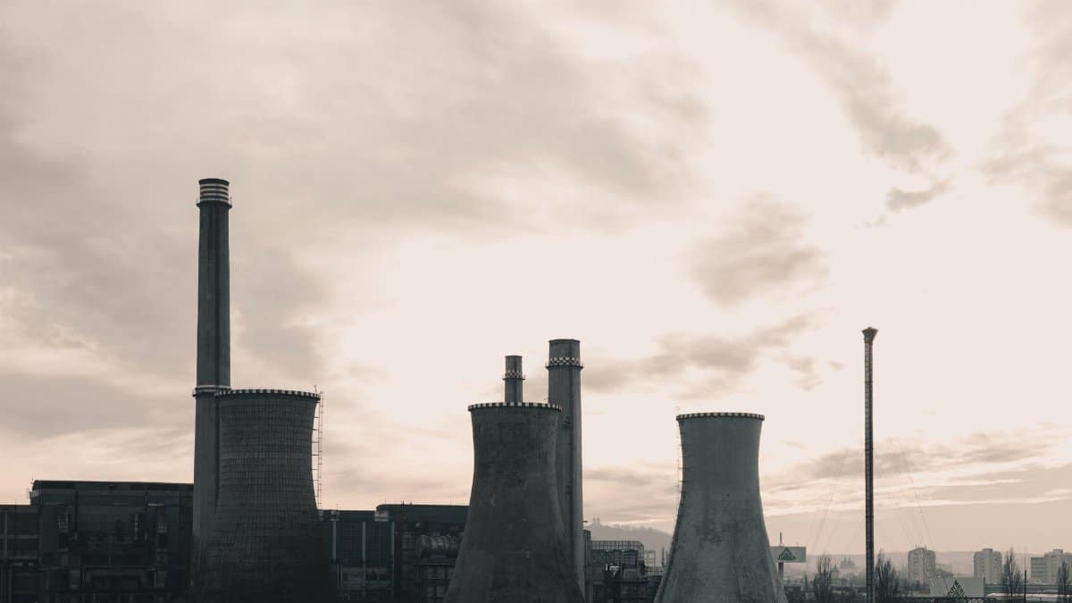 Wide-angle view of an industrial power plant with prominent cooling towers against a cloudy sky.