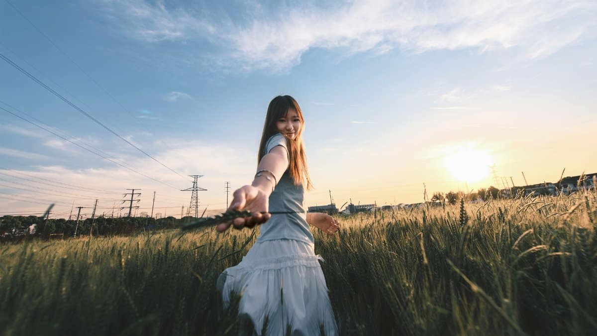 A young woman extends her hand in a wheat field during sunset, creating a warm and inviting atmosphere.