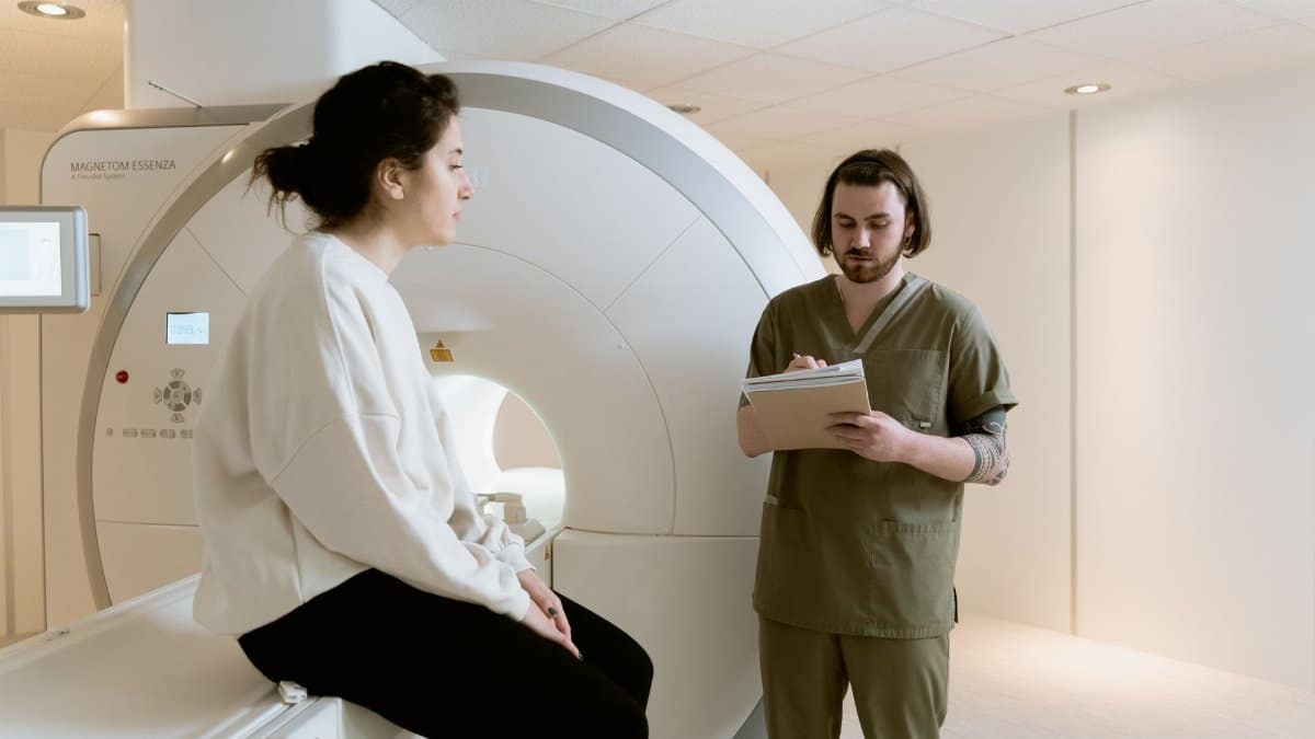 A patient undergoing an MRI scan with a healthcare technician taking notes in a medical facility.