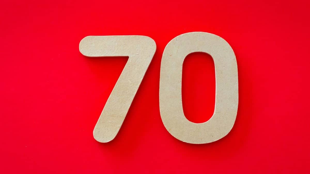 Wooden cutout of the number seventy on a vivid red background, ideal for design use.