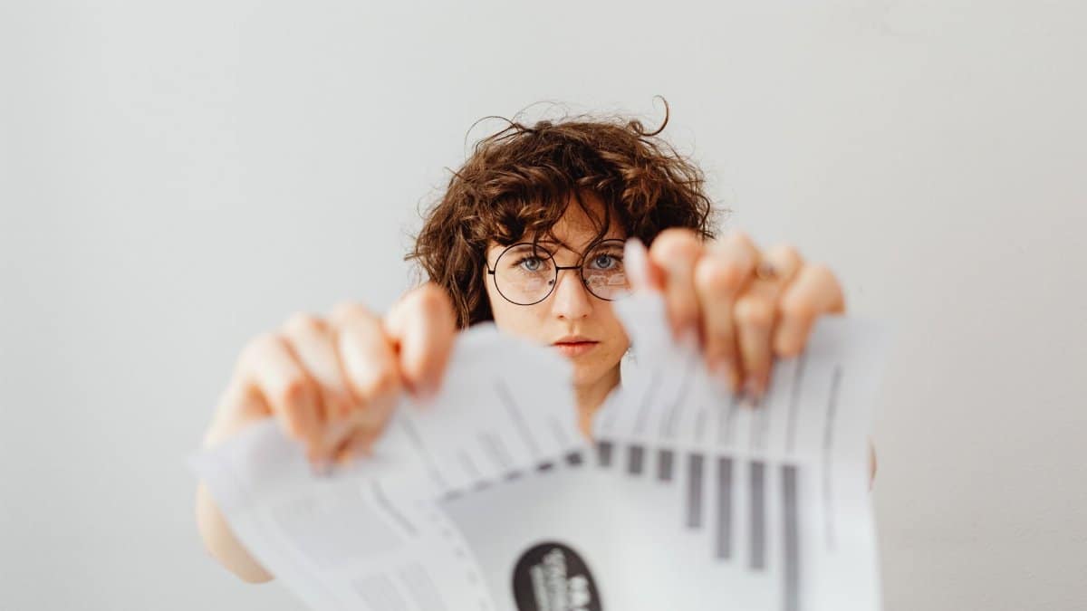 A determined woman in eyeglasses tearing a paper indoors.