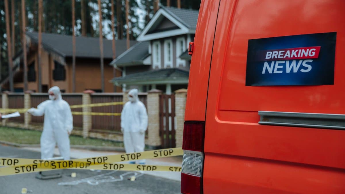 Forensic investigators in protective suits work at a marked-off crime scene near concrete houses.