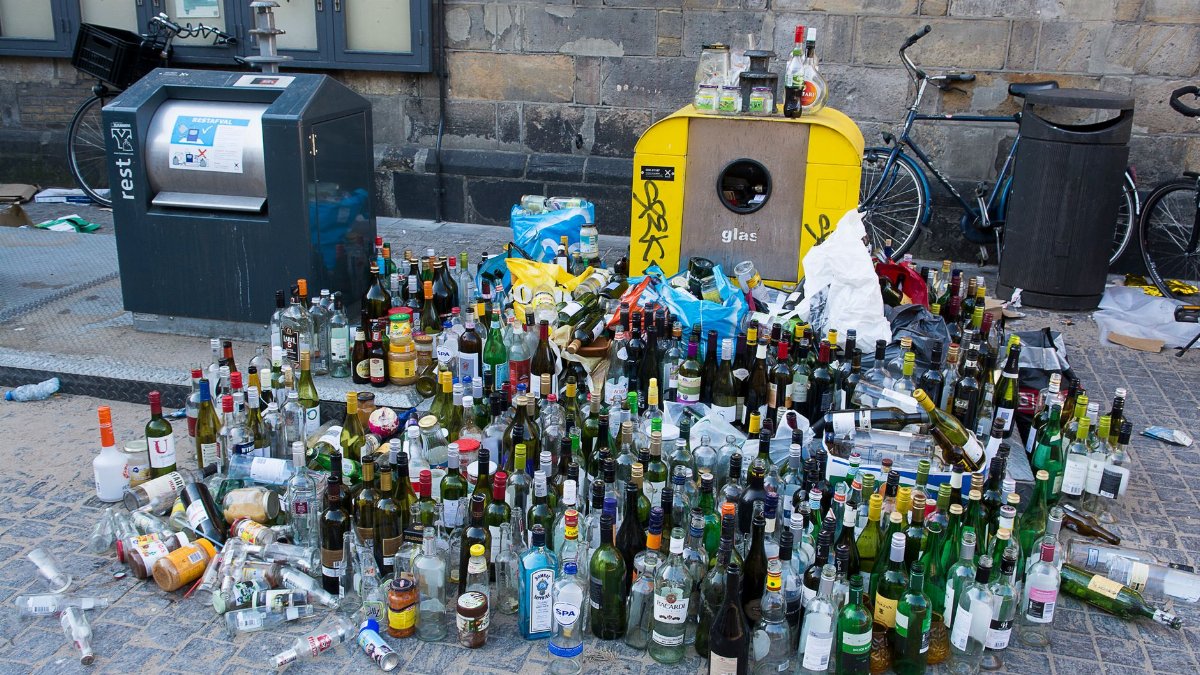 A large pile of glass bottles for recycling on a city street, emphasizing urban waste and recycling.