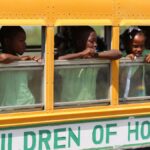 Children peering out of a yellow school bus in Dominicus, expressing hope and curiosity.