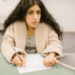 Concentrated woman writing an exam in a classroom setting, showcasing study focus.