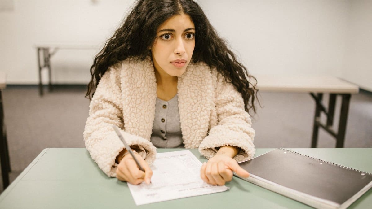 Concentrated woman writing an exam in a classroom setting, showcasing study focus.