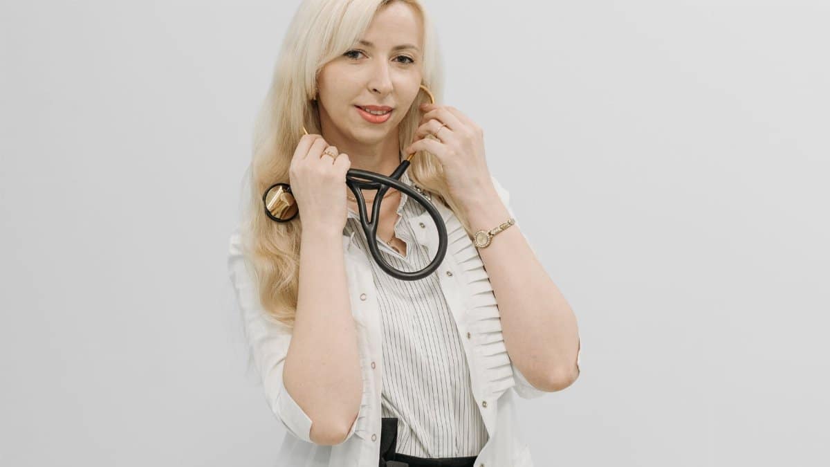 Confident female doctor posing with her stethoscope in a white coat indoors.