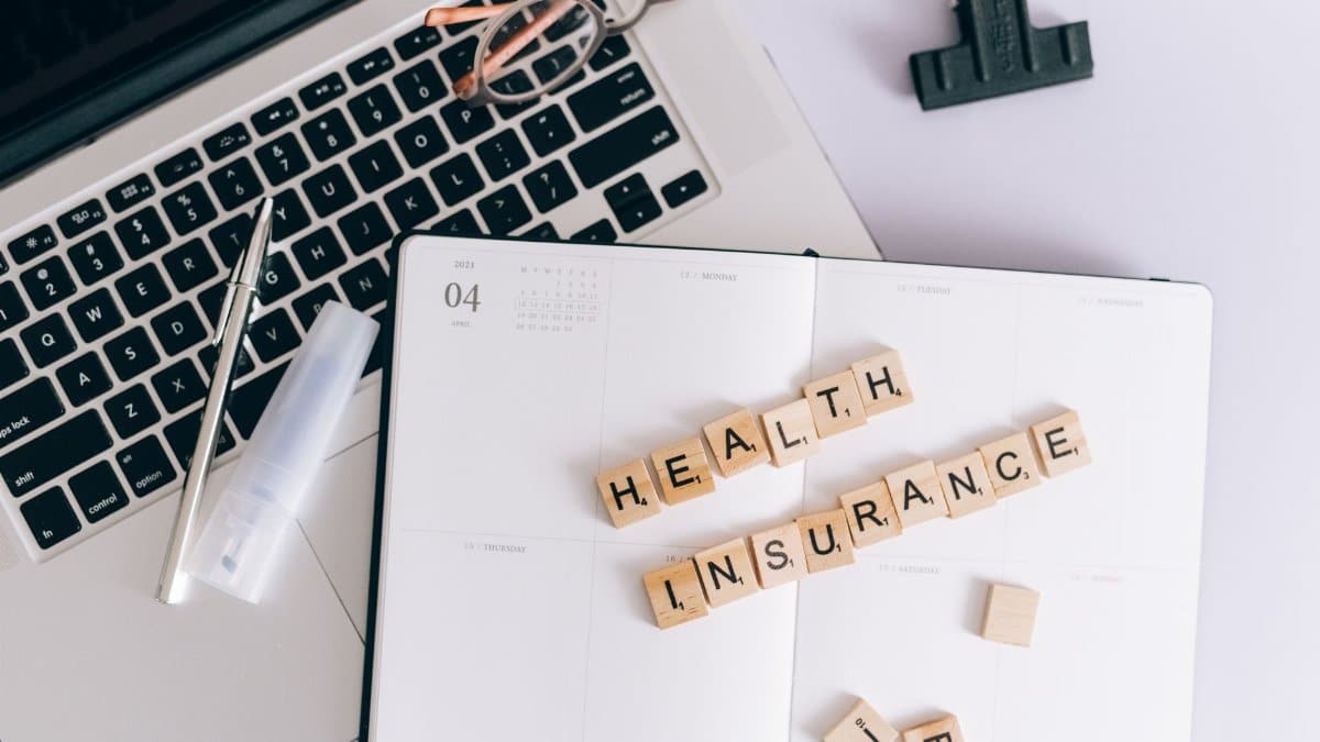 Scrabble tiles spelling health insurance on a planner next to a laptop.