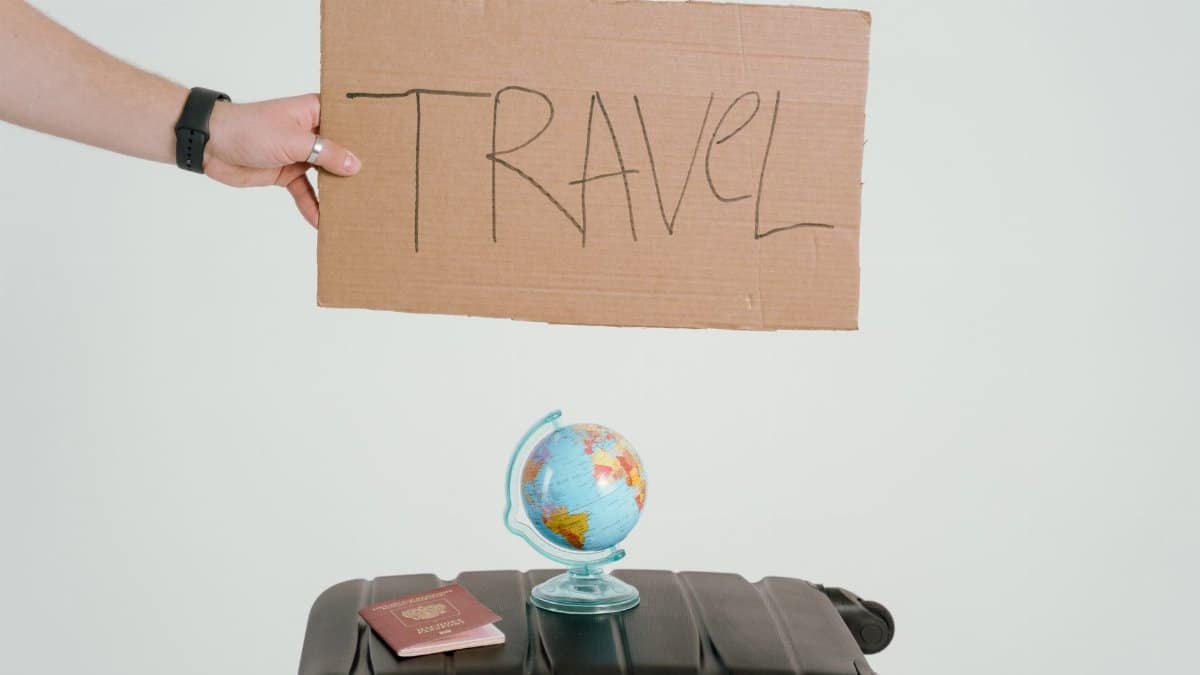 A hand holds a travel sign above a globe and suitcase, symbolizing wanderlust.