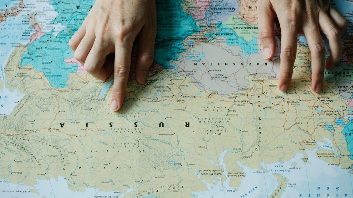 Close-up of hands pointing at Russia on a detailed world map.