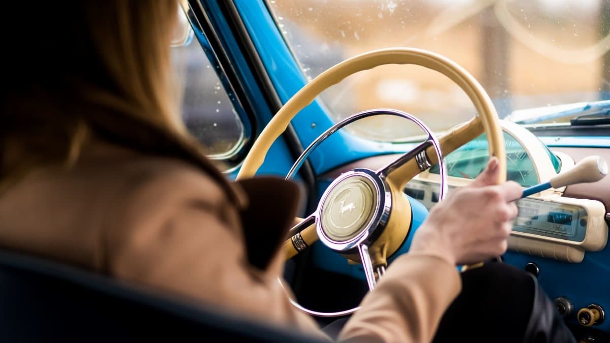 Back view of crop anonymous woman sitting on driver seat and driving retro car in daytime