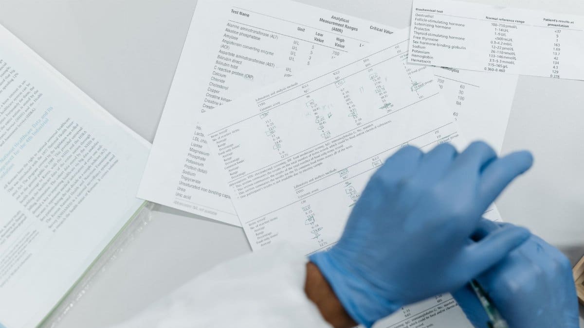Close-up of gloved hands reviewing printed lab test results on a white surface.