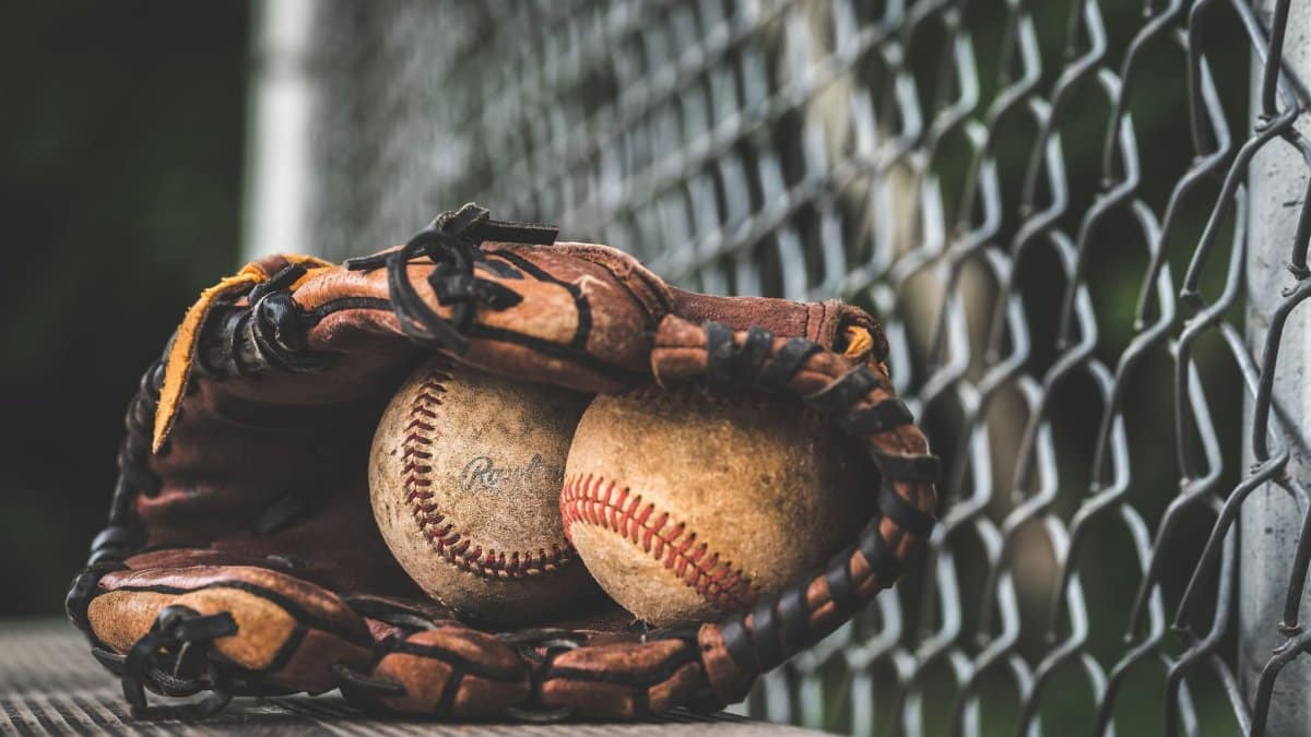 Close-up of a leather glove holding two vintage baseballs, resting near a chain-link fence.