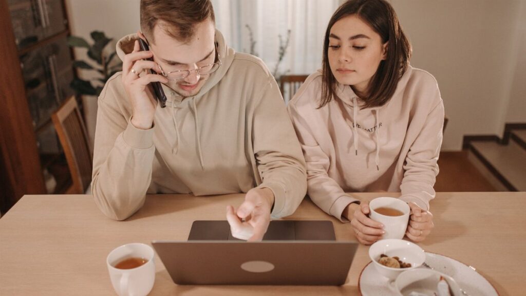 A couple enjoying coffee and online shopping together at home, using a laptop and smartphone.