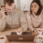 A couple enjoying coffee and online shopping together at home, using a laptop and smartphone.