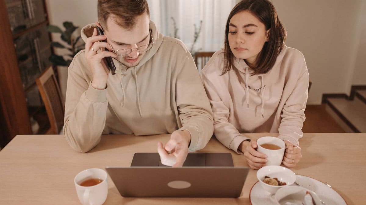 A couple enjoying coffee and online shopping together at home, using a laptop and smartphone.
