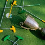 Colorful mini golf putters with a trophy on vibrant green turf, symbolizing victory.