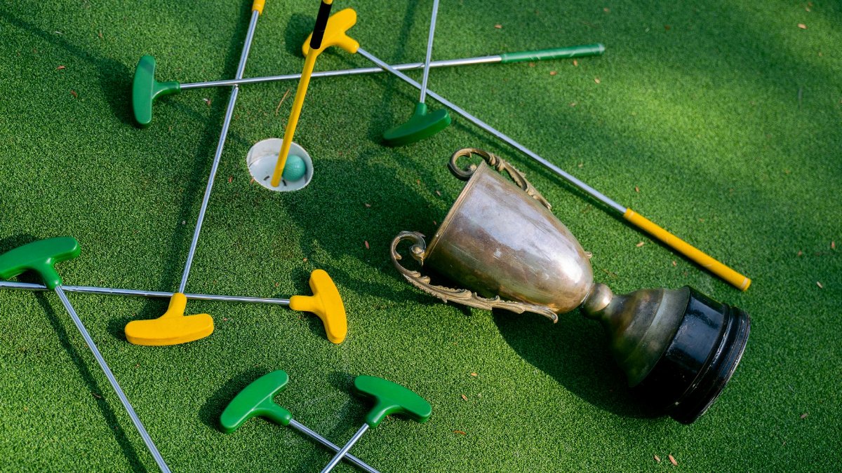 Colorful mini golf putters with a trophy on vibrant green turf, symbolizing victory.