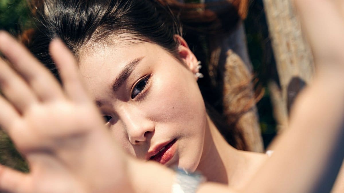 Artistic close-up of a woman's face with sunlight and hand shading.