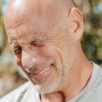Close-up of a bald, bearded man smiling with eyes closed, enjoying outdoor sunlight.