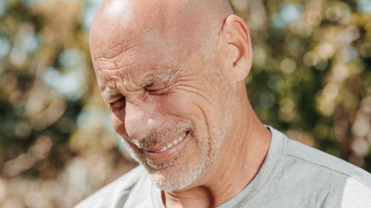 Close-up of a bald, bearded man smiling with eyes closed, enjoying outdoor sunlight.