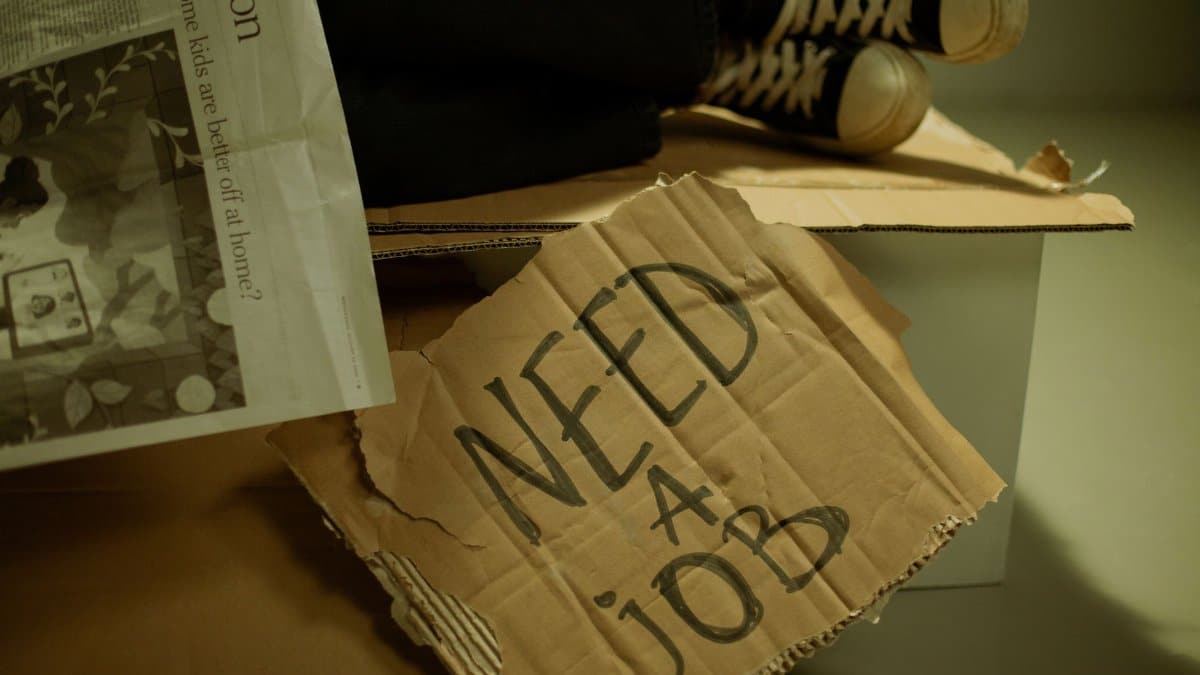 Close-up of a cardboard sign and newspaper depicting joblessness and unemployment.