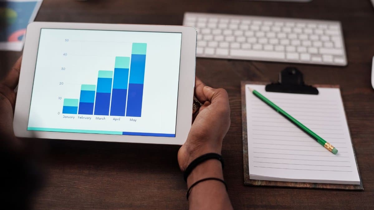 Close-up of a person holding a tablet showing growth charts on a wooden desk setup.