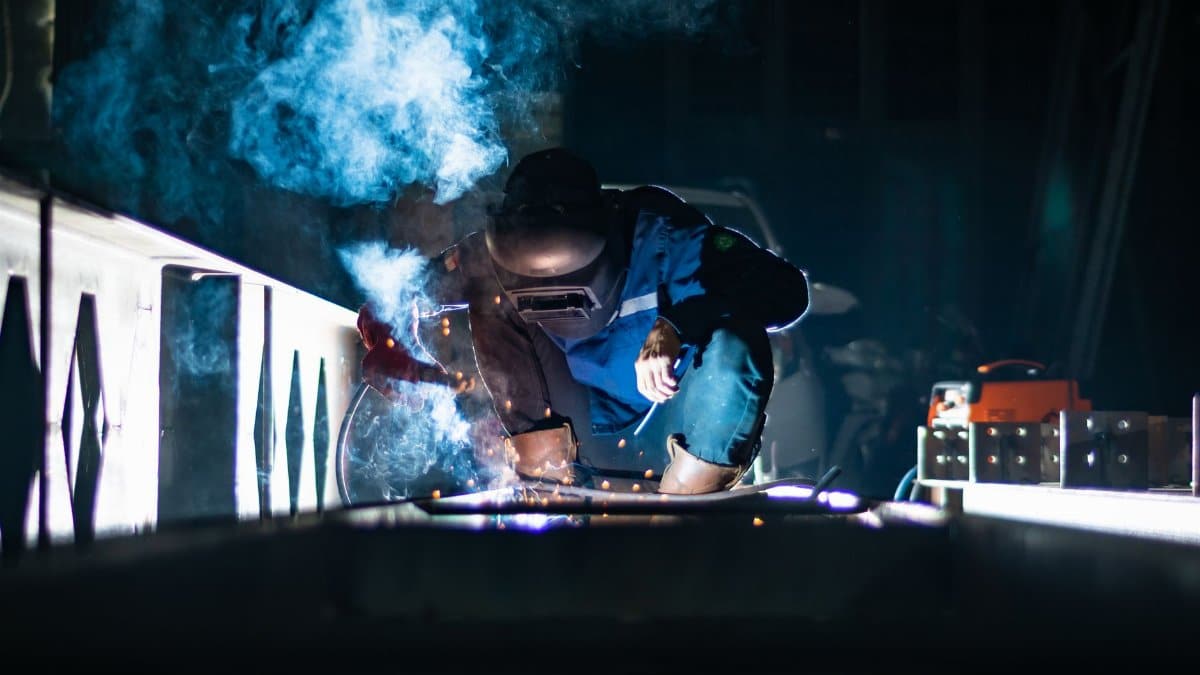 A welder working at night producing sparks and smoke in an industrial setting.