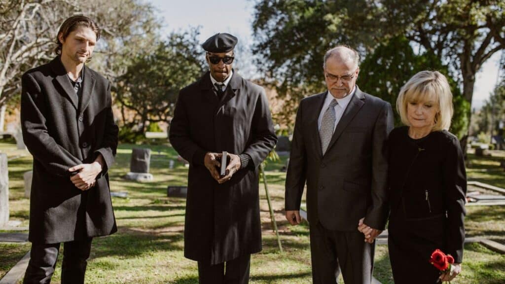 A diverse group attending a memorial service in a serene graveyard setting.
