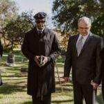 A diverse group attending a memorial service in a serene graveyard setting.