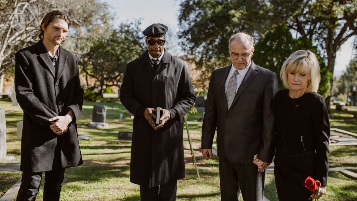 A diverse group attending a memorial service in a serene graveyard setting.