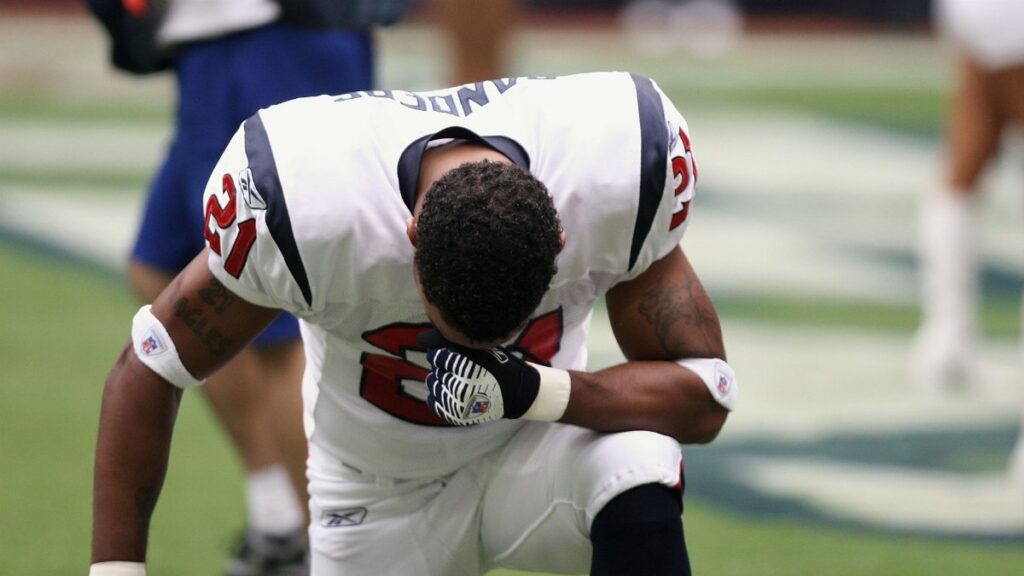 Football player in uniform kneeling before a game, displaying focus and determination.