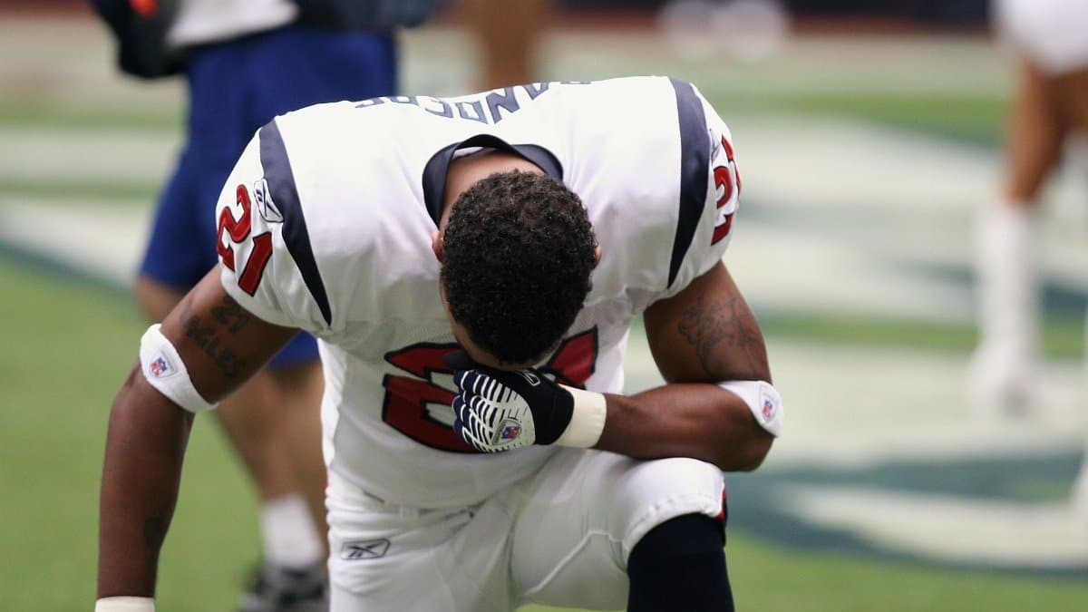 Football player in uniform kneeling before a game, displaying focus and determination.