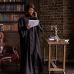 African American female judge talking on phone in a library, reviewing legal documents.