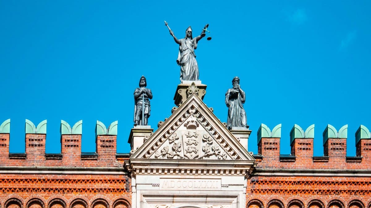 Stunning facade of Odense courthouse with Lady Justice statue under clear blue skies.