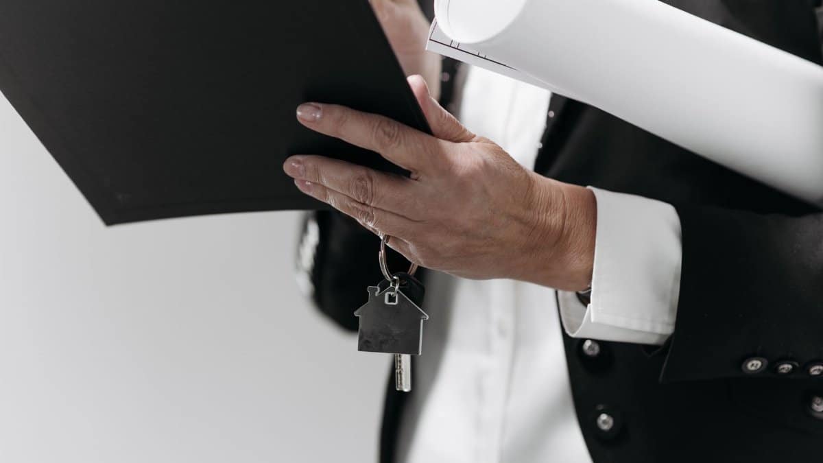 Close-up of a business professional holding a house key and architectural plans, symbolizing real estate.