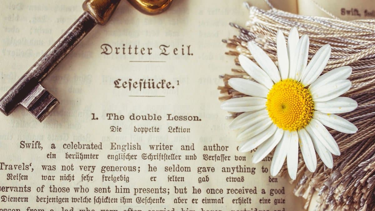 A vintage key and daisy rest on an antique book page, evoking nostalgia and elegance.