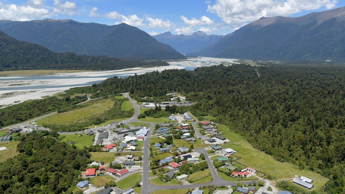 Scenic aerial view of Haast village with lush forests and mountains in the background.