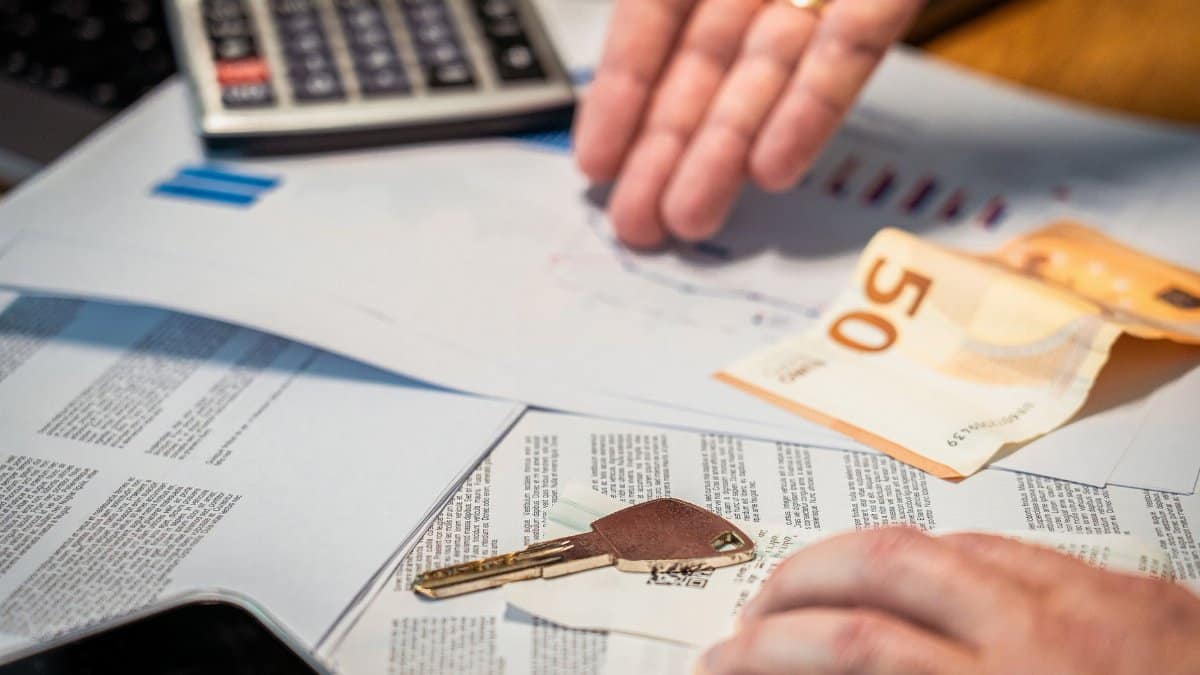 Hands examining financial documents, a 50 euro note, and a key, suggesting investment or real estate themes.