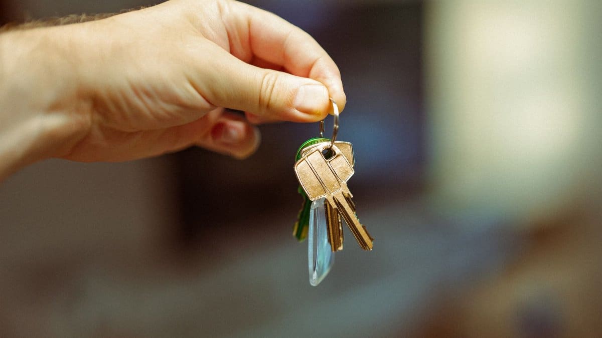 A close-up image of a hand holding a keyring with several house keys, symbolizing real estate and home ownership.