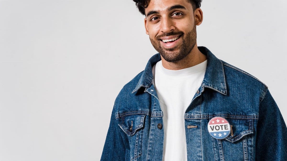 Smiling young man wearing a denim jacket with a 'vote' badge promoting civic engagement.