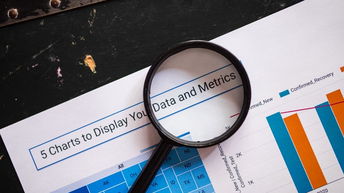 Close-up of a magnifying glass over financial data charts and metrics on printed paper.