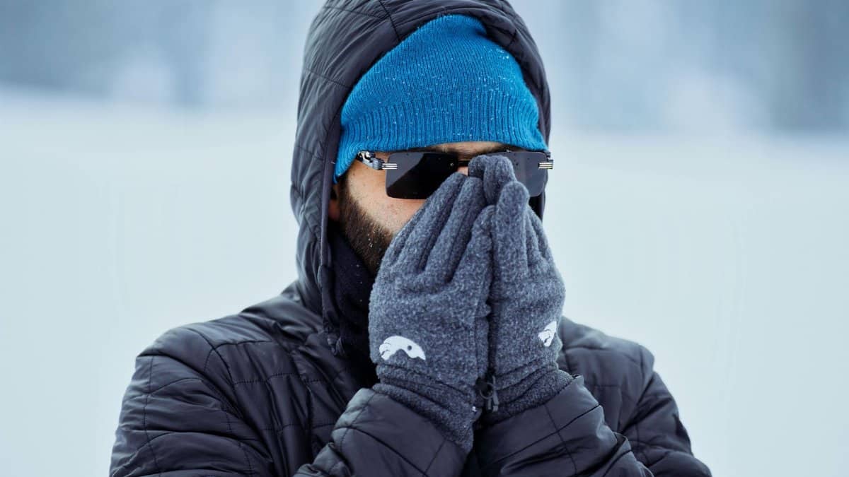 Adult male bundled in winter gear with gloves and sunglasses outdoors in cold weather.