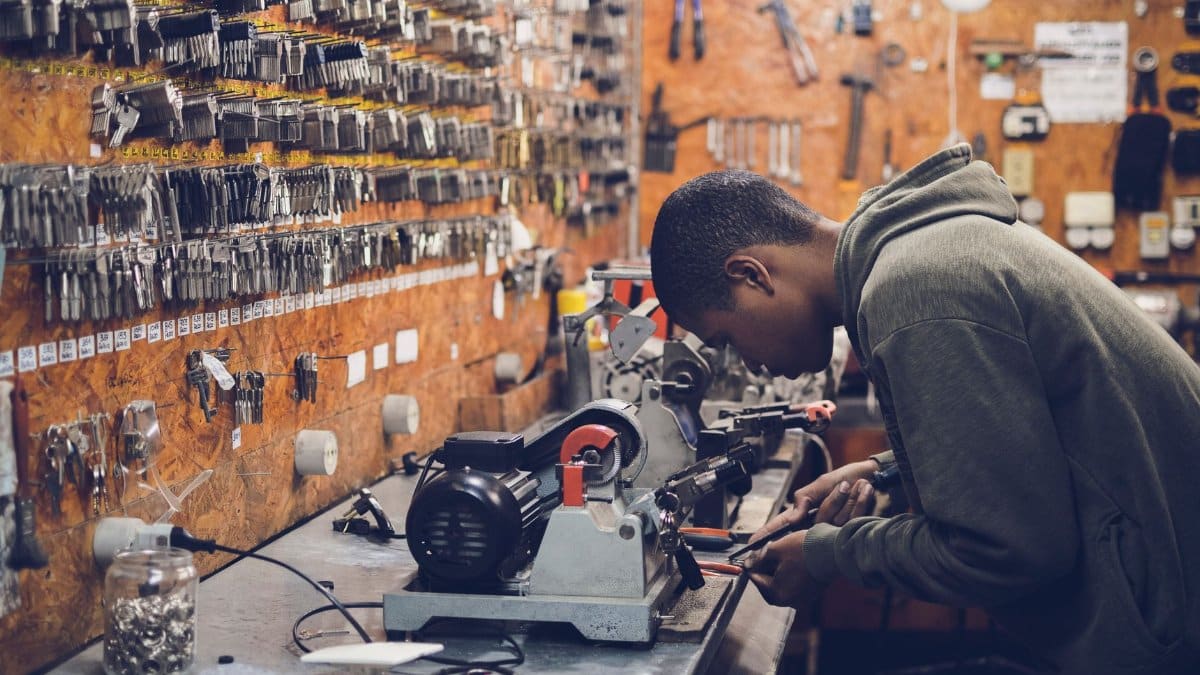 A focused craftsman works in a key-making workshop surrounded by tools and equipment.