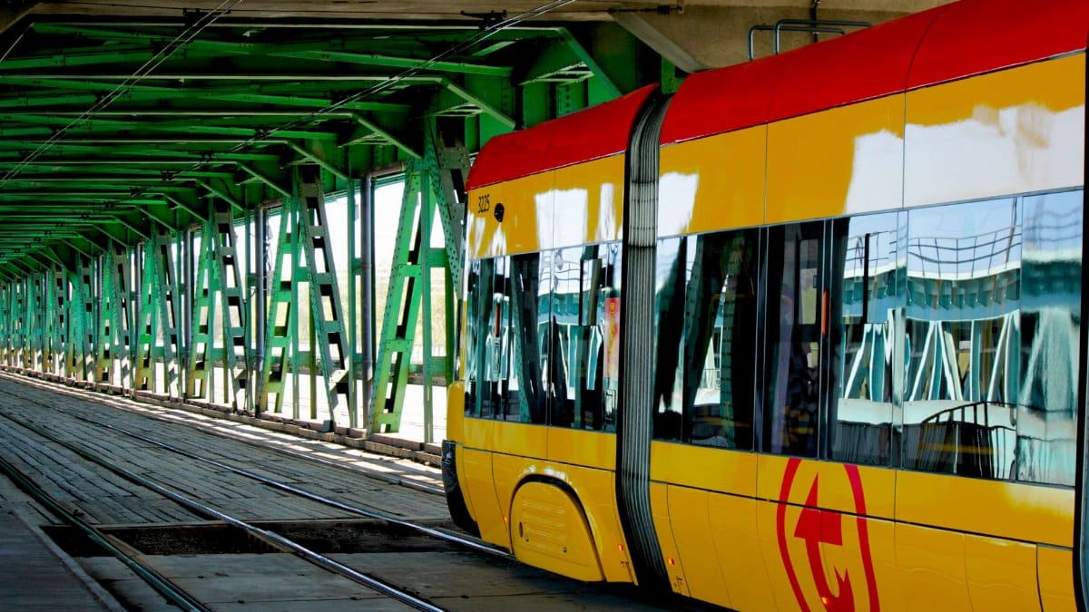 Modern yellow tram traversing an urban green steel bridge, showcasing urban transit infrastructure.