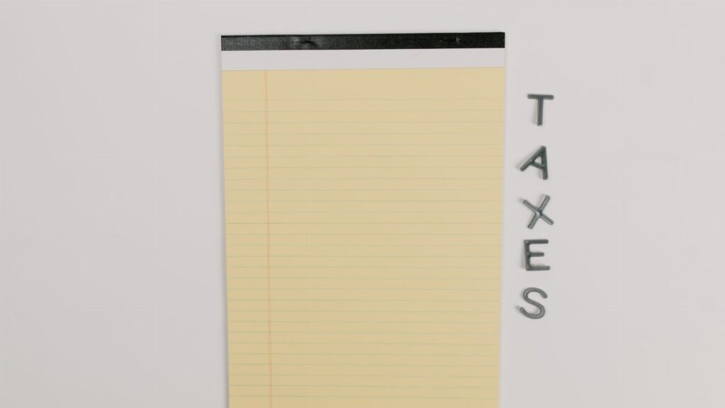 Close-up of a yellow legal pad and the word 'TAXES' on a white surface, ideal for finance themes.
